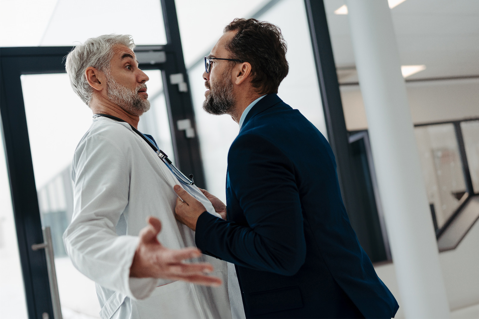 Uomo in abiti civili discute animatamente afferrando per il camice un medico all'interno di una struttura sanitaria.